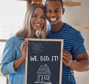 Couple holding “Our first home” sign: We did it